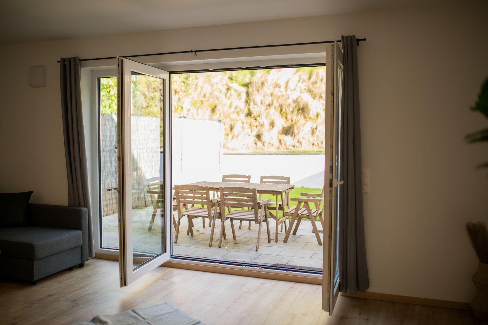 Geöffnete Terrassentür mit Blick auf Terrasse, Gartentisch für sechs und Rasen