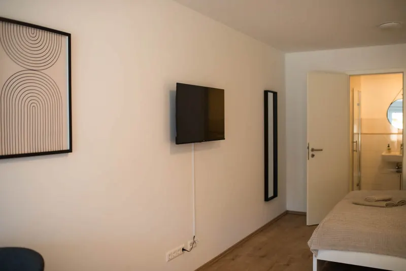Smart-TV an der Wand, daneben die Tür zum Bad
